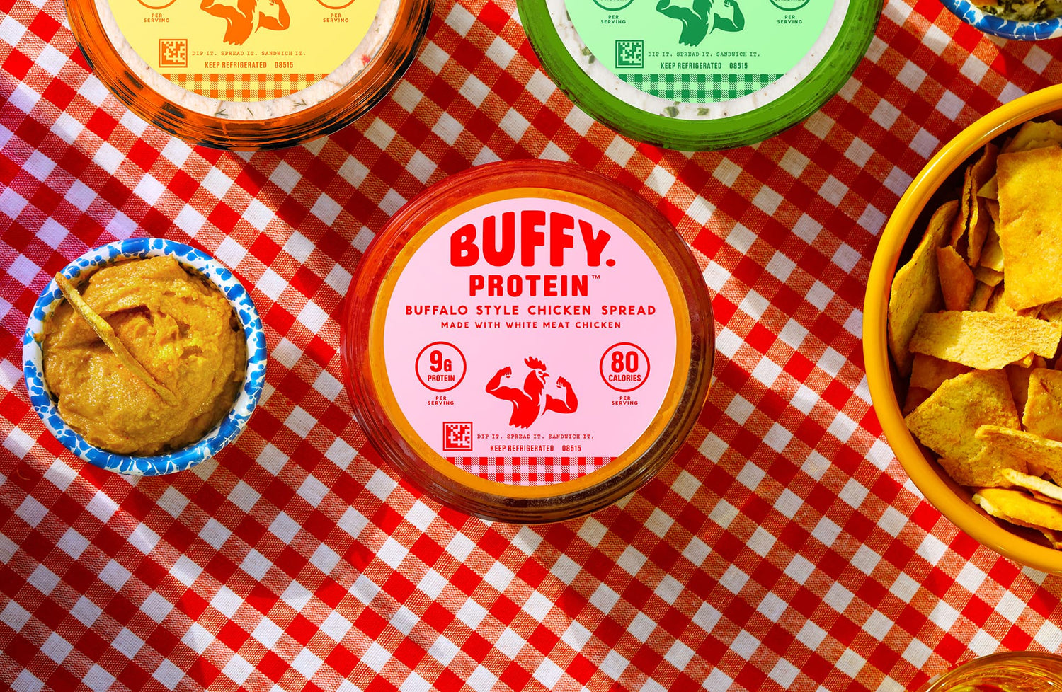 Buffy Protein spread container on a red and white checkered tablecloth with chips and dip.