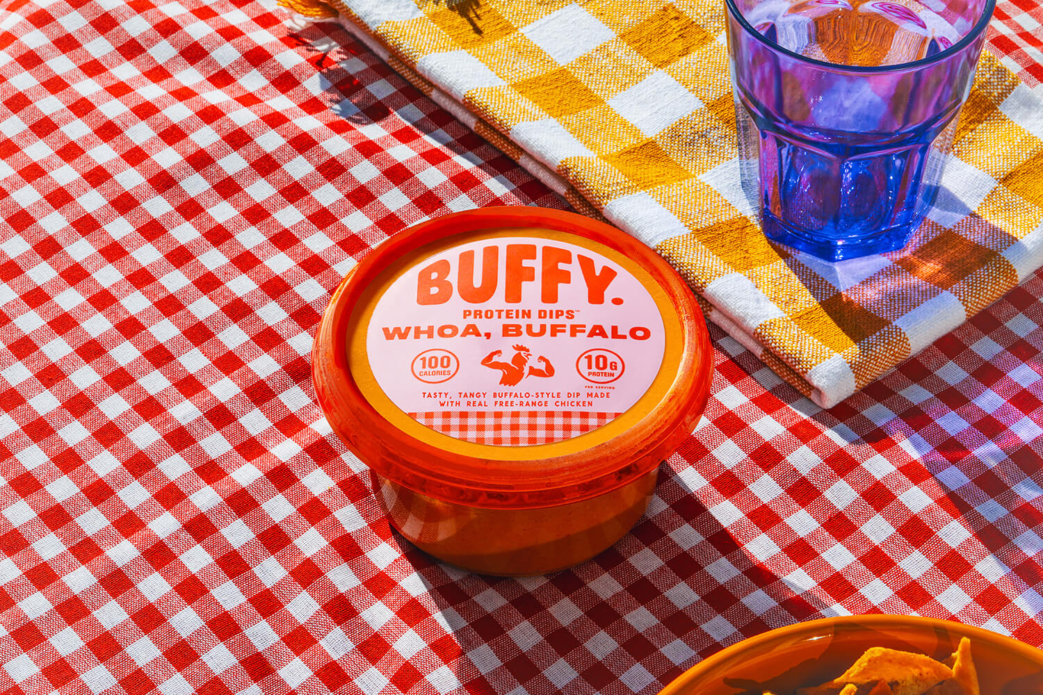 Buffy Protein Dip Whoa, Buffalo sitting on a red and white checkered picnic blanket, a red and yellow checkered napkin and blue glass are next to it, just out of frame is a bowl of chips
