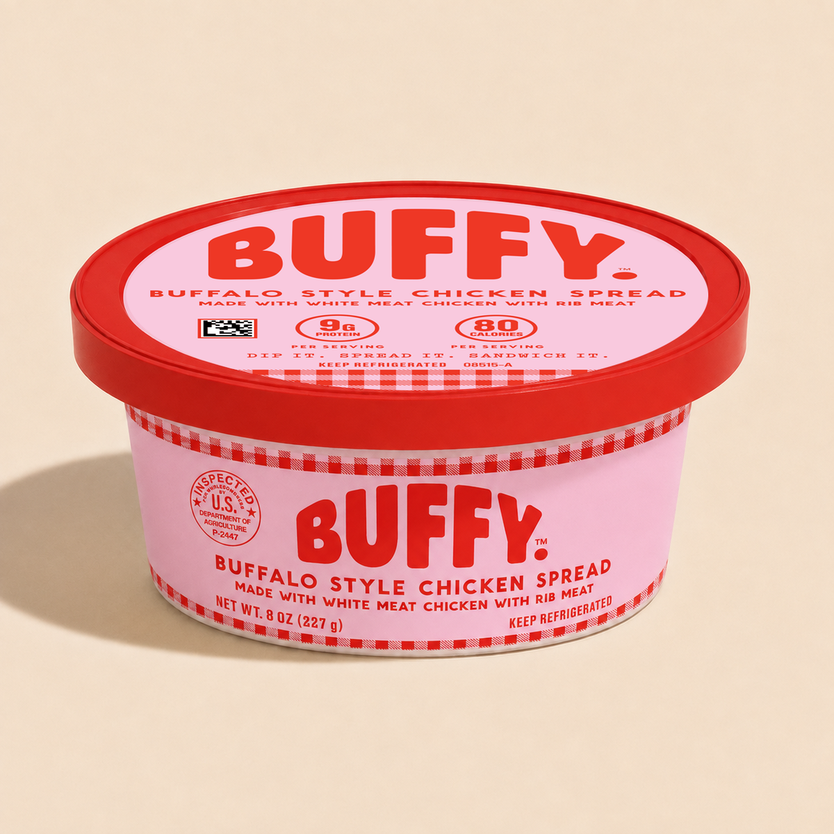 A tub of BUFFY Buffalo Style Chicken Spread with a pink container, red lid, and red-and-white gingham trim, photographed on a warm beige background.